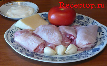 на большом блюде лежит четыре куриных бедра, один помидор, три зубчика чеснока и кусочек сыра, рядом маленькое блюдце со сметаной